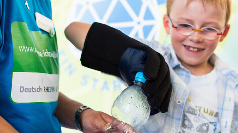 Junge mit Rheumahandschuh öffnet Wasserflasche