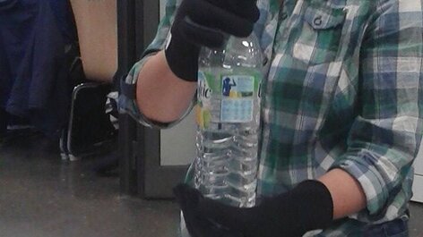 Frau mit Rheumahandschuhen hält Wasserflasche